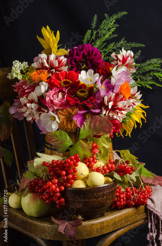 Autumn atmospheric still life with a colorful bouquet of garden flowers, red berries, apples, autumn leaves on a black background.
