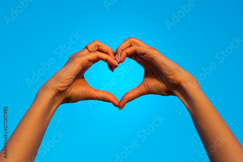 Young woman hands making heart shape symbol of love isolated on blue sky. Girl falls in love. Valentine card ideas