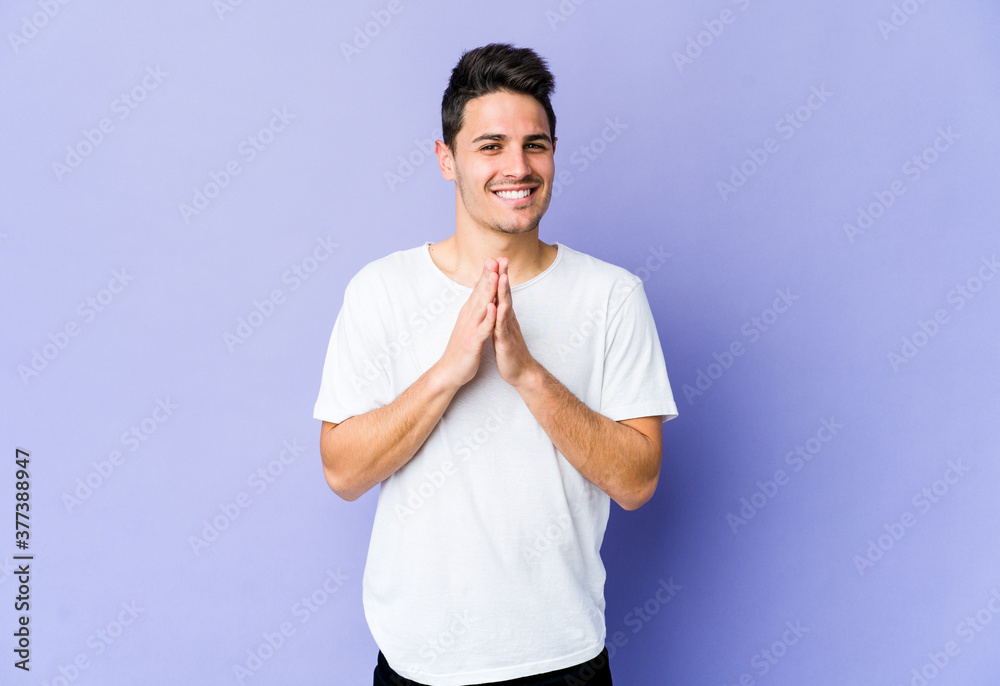 Young caucasian man isolated on purple background holding hands in pray near mouth, feels confident. Young caucasian man isolated on purple background holding hands in pray near mouth, feels confident.