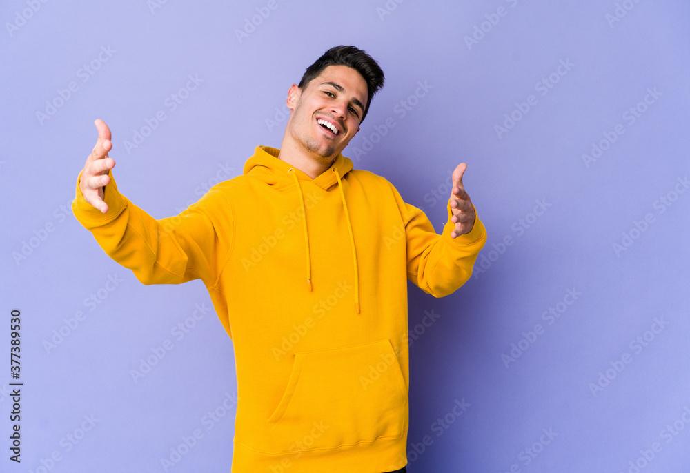 Fototapeta premium Young caucasian man isolated on purple background feels confident giving a hug to the camera.