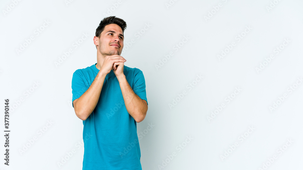 Young caucasian man isolated on white background keeps hands under chin, is looking happily aside. Young caucasian man isolated on white background keeps hands under chin, is looking happily aside.
