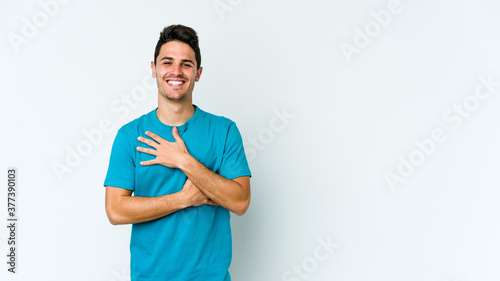 Young caucasian man isolated on white background laughs happily and has fun keeping hands on stomach.