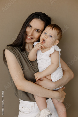 Woman in light clothes have fun with cute child baby girl. Mother, little kid daughter isolated on pastel wall background, studio portrait. Mother's Day love family, parenthood childhood concept