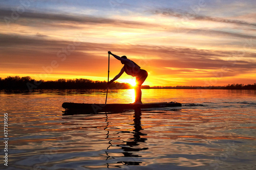 Silhouette of woman paddle on stand up paddle boarding (SUP) on quiet winter or autumn river at sunset. Colorful sunset over the river © watcherfox