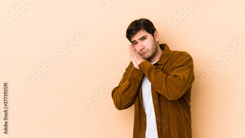 Young man isolated on beige background yawning showing a tired gesture covering mouth with hand.