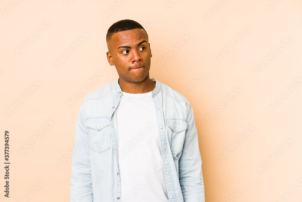 Young latin man isolated on beige background confused, feels doubtful and unsure. Young latin man isolated on beige background confused, feels doubtful and unsure.