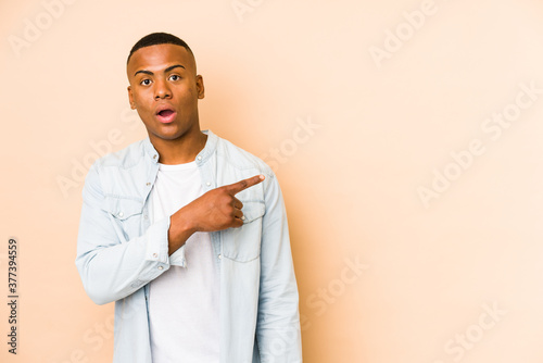 Young latin man isolated on beige background pointing to the side