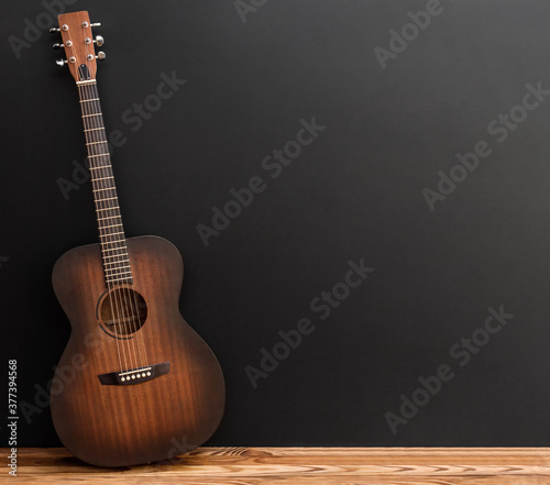 Wooden classical acoustic guitar stands near blackwall.