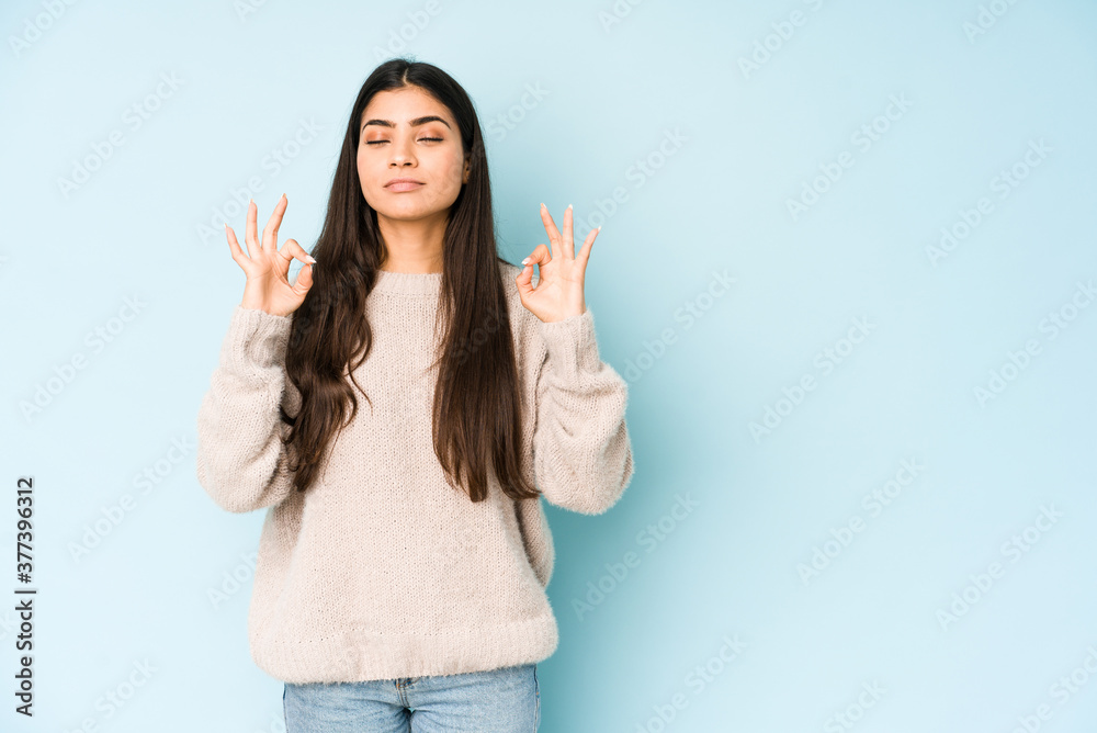 Young indian woman isolated on blue background relaxes after hard working day, she is performing yoga. Young indian woman isolated on blue background relaxes after hard working day, she is performing yoga.