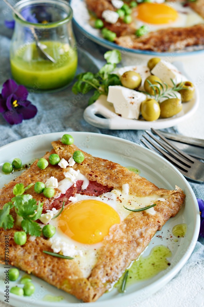 Breton traditional pancake made from buckwheat flour with ham, cheese, egg, feta, green peas and green butter. Breakfast of buckwheat thin pancakes with fried eggs, ham and cheese, eggs for breakfast