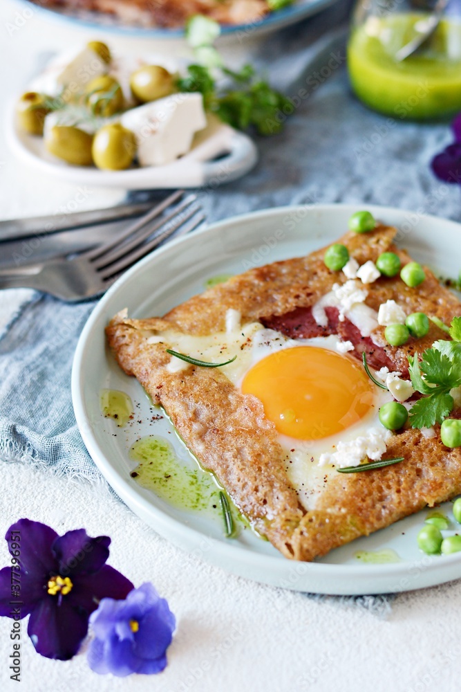 Breton traditional pancake made from buckwheat flour with ham, cheese, egg, feta, green peas and green butter. Breakfast of buckwheat thin pancakes with fried eggs, ham and cheese, eggs for breakfast