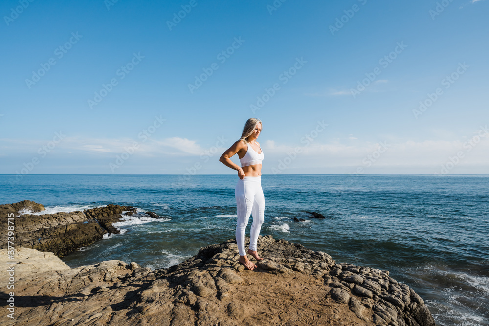 Female athlete standing on rocky beach, looking towards the sun Female athlete standing on rocky beach, looking towards the sun