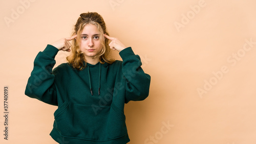 Young caucasian woman isolated on beige background focused on a task, keeping forefingers pointing head. © Asier