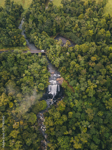 Aerial shot of Zillie Falls sourranded by lush green forest while a van driving through a bridge crossing in Tropical Queensland, Australia photo