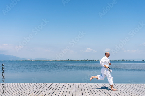 A man practices martial arts running on a wooden walkway by the sea photo