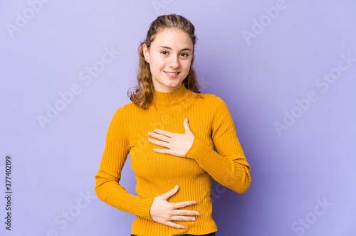 Young caucasian woman on purple background laughs happily and has fun keeping hands on stomach.