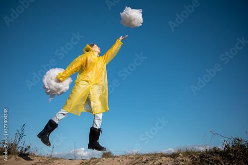 a woman in a yellow raincoat jumps behind a cloud of padding polyester