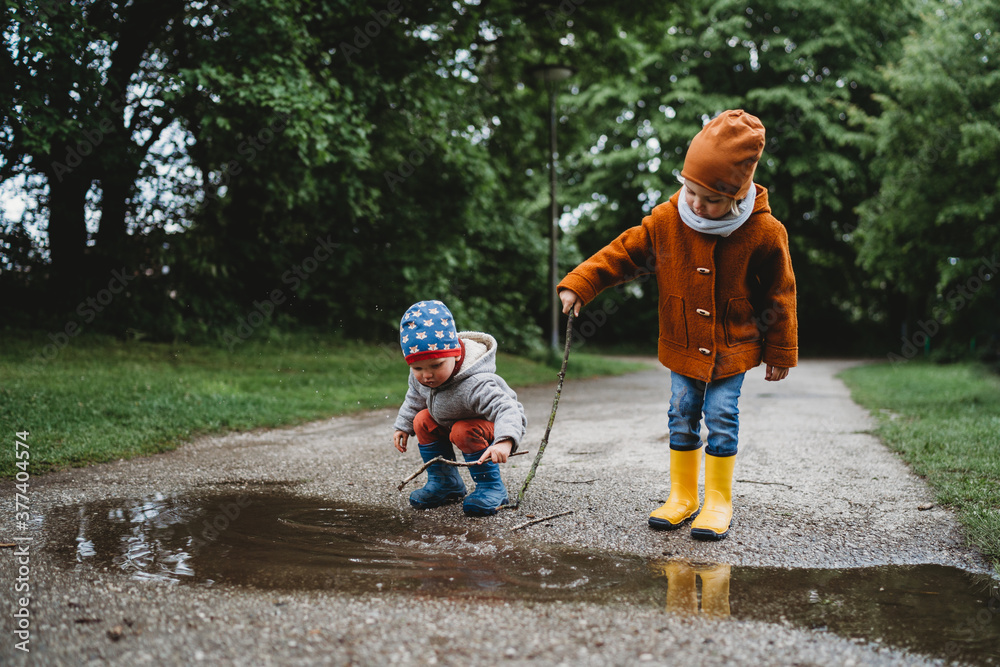 Front view of young male kids playing with sticks in a puddle in park Front view of young male kids playing with sticks in a puddle in park