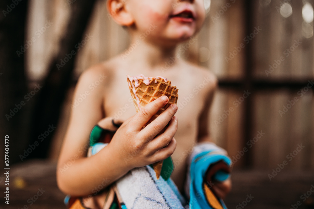 Close up of young boy holding dripping ice cream cone in summer