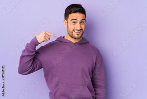 Young caucasian man isolated on purple background person pointing by hand to a shirt copy space, proud and confident © Asier