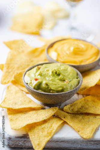 Nachos chips in a bowl with sauces guacamole and cheese, dip variety, over white stone background.