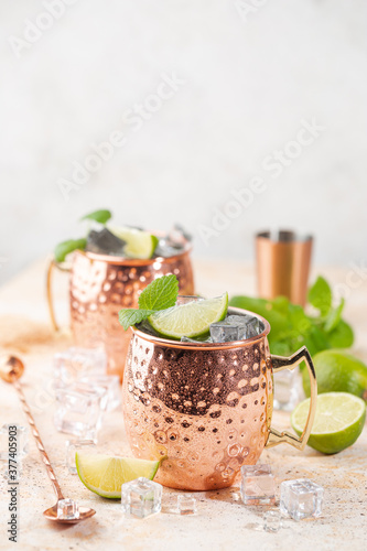 Cold Moscow Mules cocktail with ginger beer, vodka, lime. White stone background.