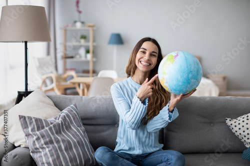 Young female tourist holding globe, pointing with index finger to desirable destination of her trip. Planning vacation.