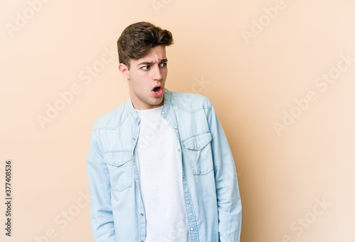 Young caucasian man isolated on beige background being shocked because of something she has seen.