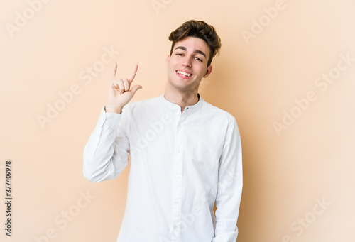 Young caucasian man isolated on beige background showing a horns gesture as a revolution concept.