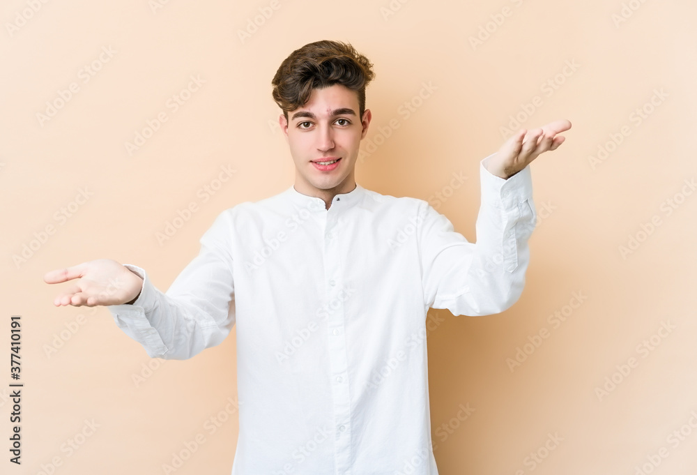 Young caucasian man isolated on beige background makes scale with arms, feels happy and confident.