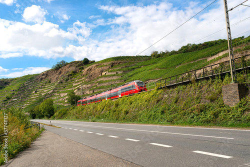 A red passenger train driving alongside an empty motorway next to the hills of a vineyard in Germany. photo