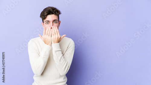 Young caucasian man isolated on purple background shocked, covering mouth with hands, anxious to discover something new.