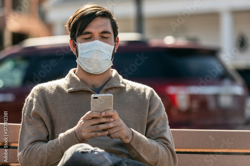 Virus: Man Wearing Medical Mask Uses Phone While Sitting On Benc photo