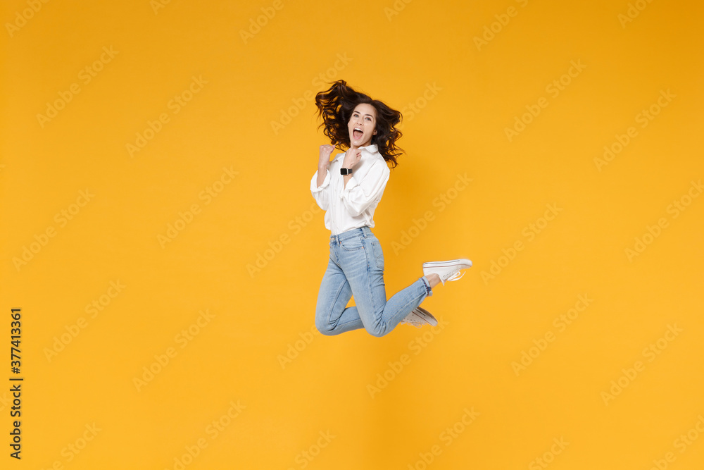 Side view of excited young brunette business woman in white shirt posing isolated on yellow background. Achievement career wealth business concept. Mock up copy space. Jumping, doing winner gesture. Side view of excited young brunette business woman in white shirt posing isolated on yellow background. Achievement career wealth business concept. Mock up copy space. Jumping, doing winner gesture.