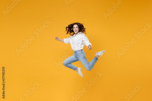 Cheerful young brunette business woman in white shirt posing isolated on yellow background in studio. Achievement career wealth business concept. Mock up copy space. Jumping, spreading hands and legs.