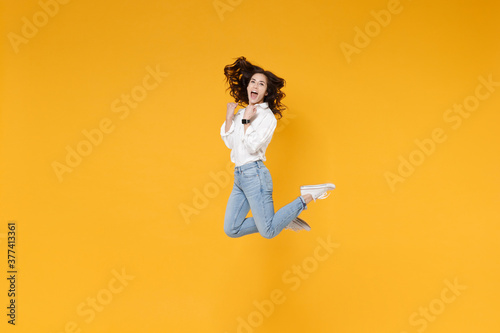 Side view of excited young brunette business woman in white shirt posing isolated on yellow background. Achievement career wealth business concept. Mock up copy space. Jumping, doing winner gesture.