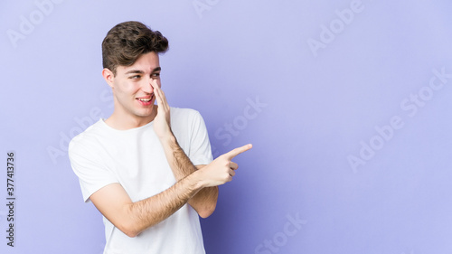 Young caucasian man isolated on purple background saying a gossip, pointing to side reporting something.
