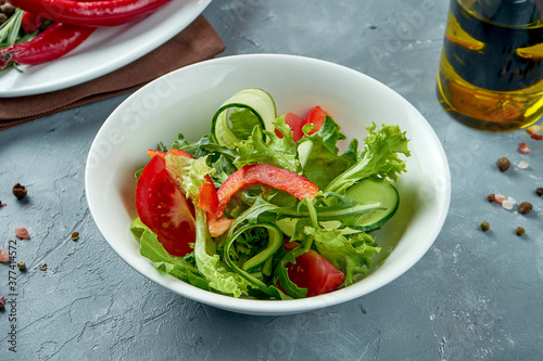 Light vegetable salad of lettuce, tomatoes and cucumber in a white bowl on a gray background. Veggie salad