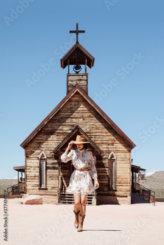Stylish cowgirl walks in front of old church in the desert.