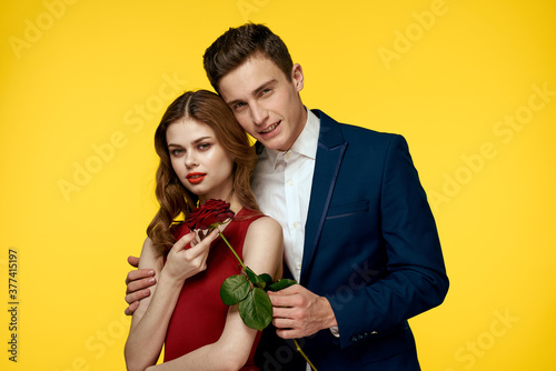 lovers man and woman with a red rose in their hands hugging on a yellow background romance relationship love family