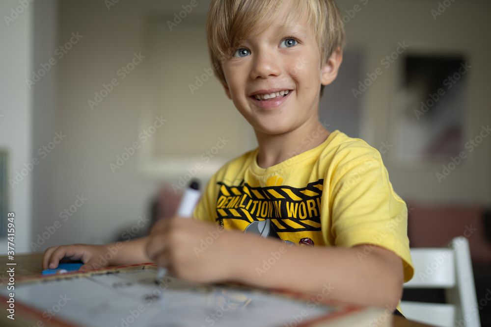 Happy smiling little boy drawing with marker pens