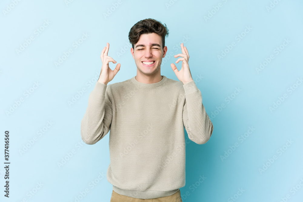 Young caucasian man isolated on blue background crossing fingers for having luck Young caucasian man isolated on blue background crossing fingers for having luck
