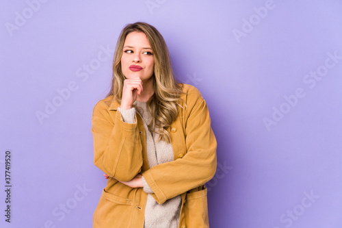 Young caucasian woman isolated on purple background looking sideways with doubtful and skeptical expression.