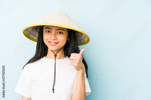 Young chinese woman wearing a vietnamese hay isolated smiling and pointing aside, showing something at blank space.