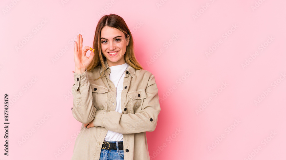Young caucasian woman isolated on pink background winks an eye and holds an okay gesture with hand. Young caucasian woman isolated on pink background winks an eye and holds an okay gesture with hand.