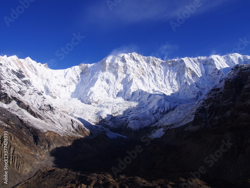 A mountain climber standing in front of a snow-covered Himalayas in the blue skies  ABC  Annapurna Base Camp  Trek  Annapurna  Nepal