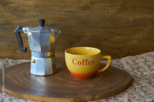 Geyser coffee maker on a wooden tray. There's a cup of coffee next to it. Dark background