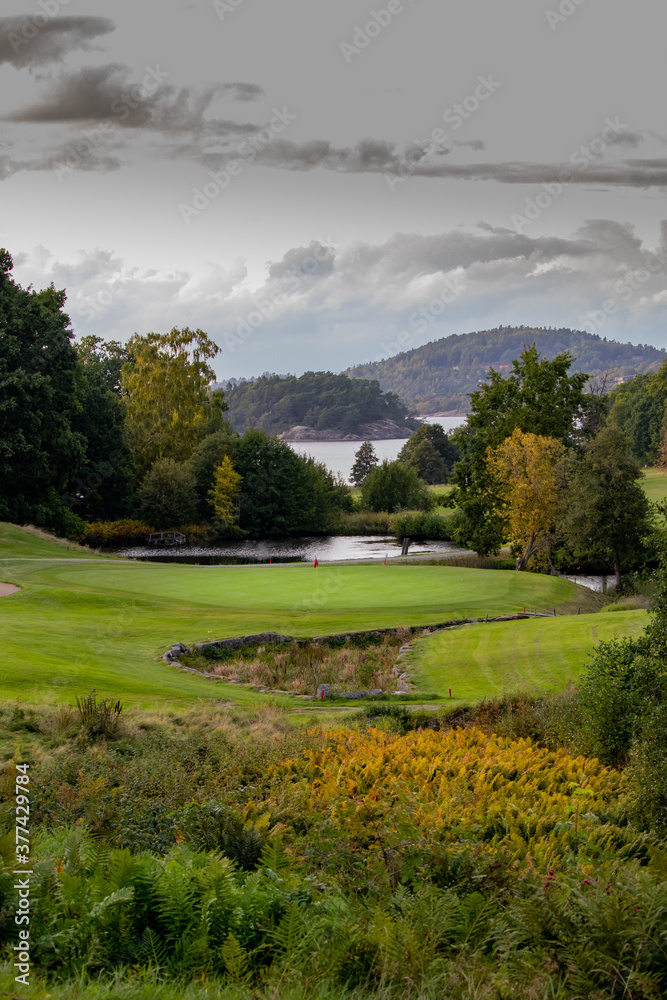 Stunning landscape of a golf hole in Sweden. Vegetation in the foreground, green in the middle, a pond and finally the ocean with islands in the background. There are autumn colors in the trees. Stunning landscape of a golf hole in Sweden. Vegetation in the foreground, green in the middle, a pond and finally the ocean with islands in the background. There are autumn colors in the trees.