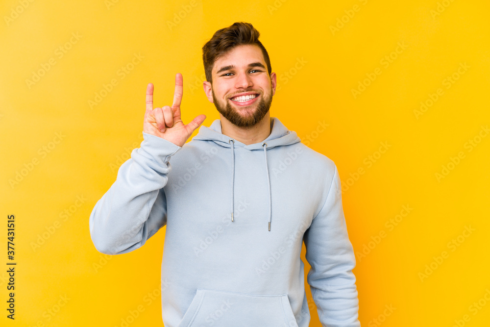 Young caucasian man isolated on yellow background showing a horns gesture as a revolution concept. Young caucasian man isolated on yellow background showing a horns gesture as a revolution concept.