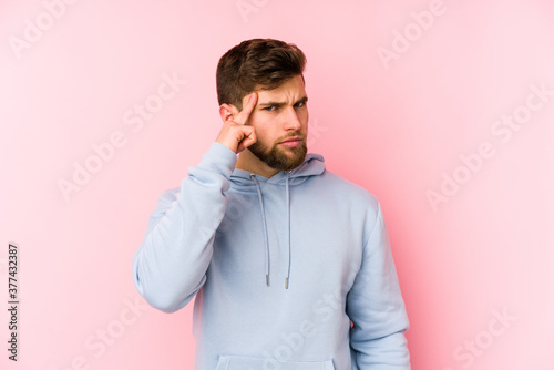Young caucasian man isolated on pink background pointing temple with finger, thinking, focused on a task.